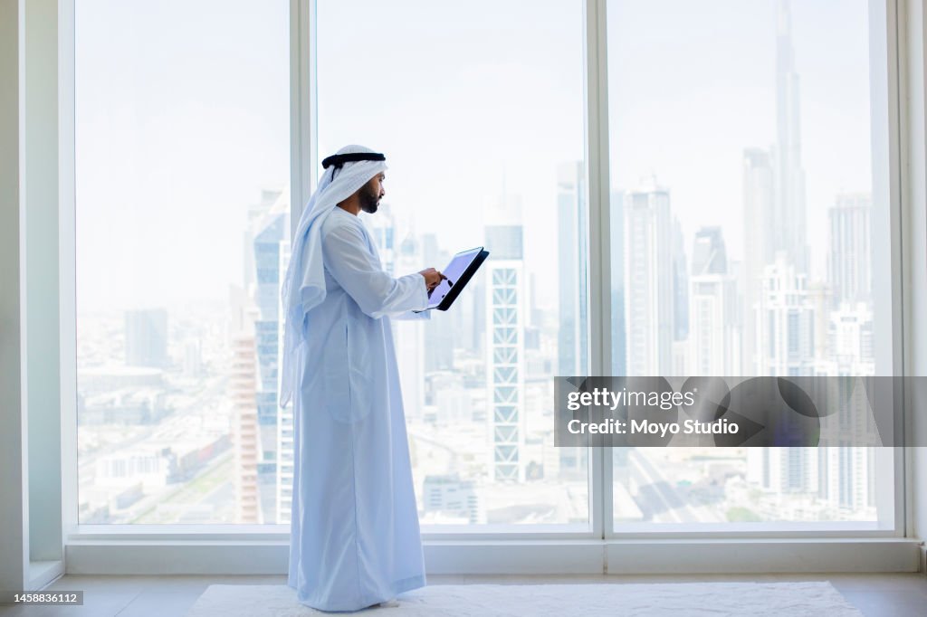 Side view of Arab businessman using digital tablet beside window in modern office