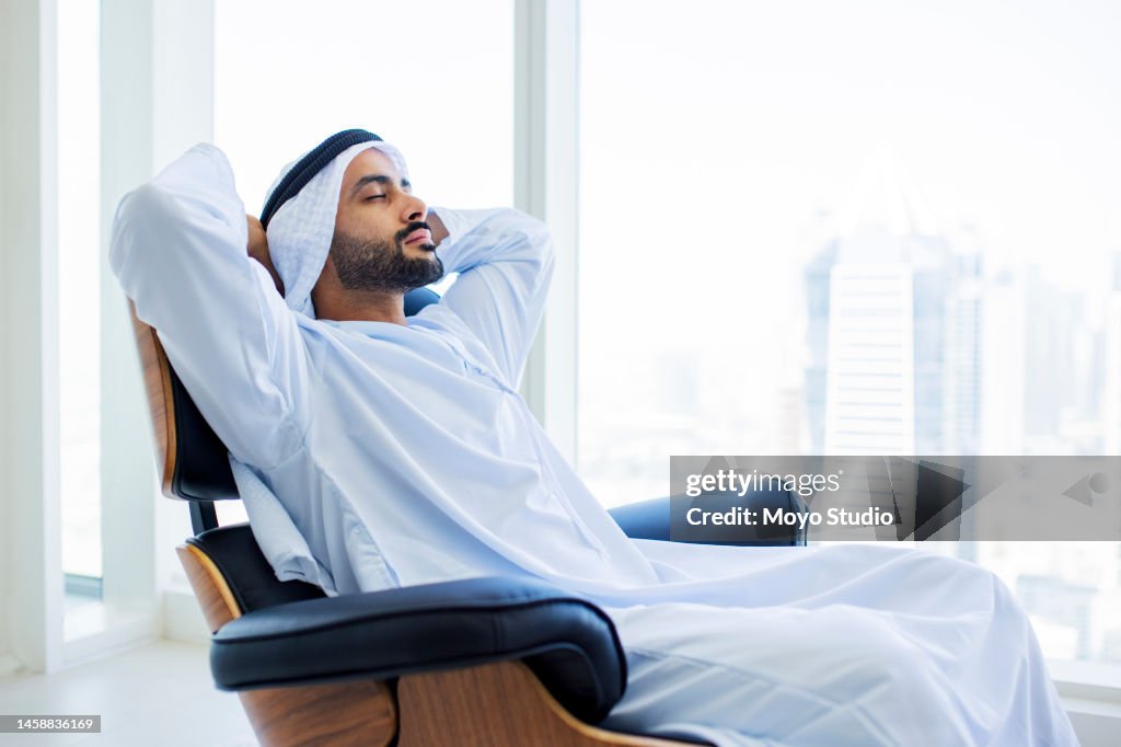Arab man with beard relaxing on modern armchair in office with city view