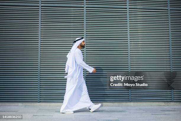 side view of bearded arab businessman walking past metal grille - arab man walking stock pictures, royalty-free photos & images