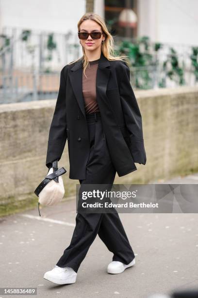 Guest wears black sunglasses, silver earrings, a black transparent t-shirt, a black blazer jacket, black high waist large suit pants, a white sheep...