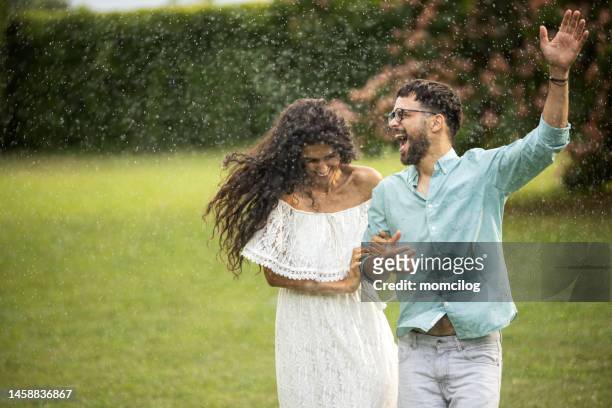 beautiful couple running and having fun while raining outdoor - couples kissing shower stockfoto's en -beelden