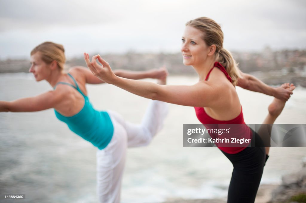 Two women doing yoga pose by the sea