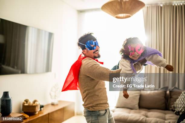 father and daughter playing superhero in the living room at home - superhero girl stock pictures, royalty-free photos & images