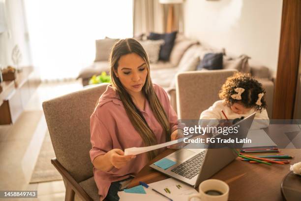young woman working while her daughter draws beside her at home - financial planner stockfoto's en -beelden