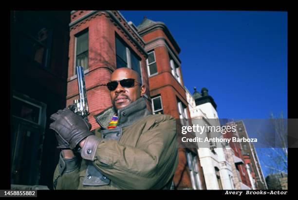 Low-angle portrait of American actor Avery Brooks, a pistol in his gloved hands, as he poses outdoors, circa 1980s.