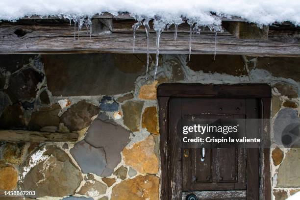 close-up of a stone and wood cabin with snow and ice on the roof. - mountain village stock pictures, royalty-free photos & images