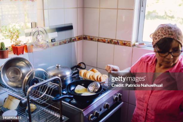 mapuche woman frying sopaipillas in a frying pan, in the kitchen at home. typical chilean food. - chilean ethnicity stock pictures, royalty-free photos & images