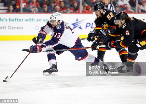 Johnny Gaudreau of the Columbus Blue Jackets battles for the puck with MacKenzie Weegar of the Calgary Flames and Chris Tanev of the Calgary Flames...