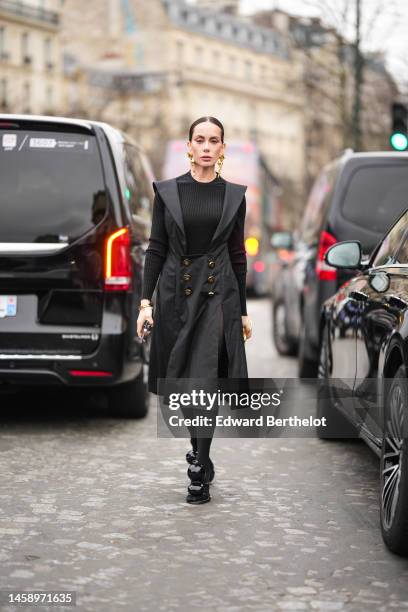 Sira Pevida wears gold face pattern large pendant earrings from Schiaparelli, a black ribbed wool pullover, a black long V)neck / shoulder pads /...