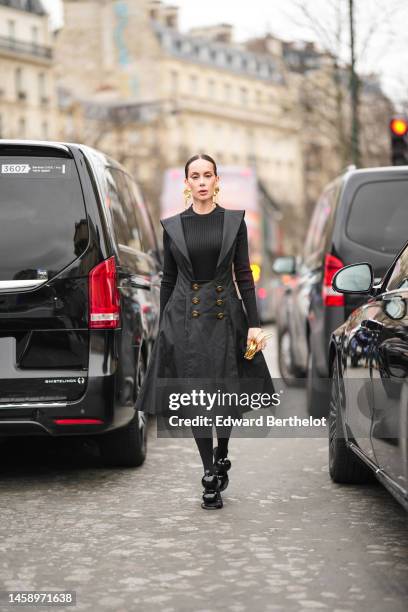 Sira Pevida wears gold face pattern large pendant earrings from Schiaparelli, a black ribbed wool pullover, a black long V)neck / shoulder pads /...