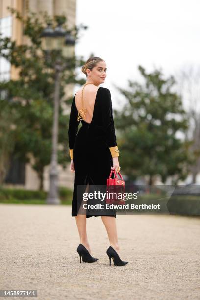 Valentina Ferragni wears a gold large pendant chain back necklace, a black velvet with gold sleeves long midi dress, a gold oversized ring, a red...