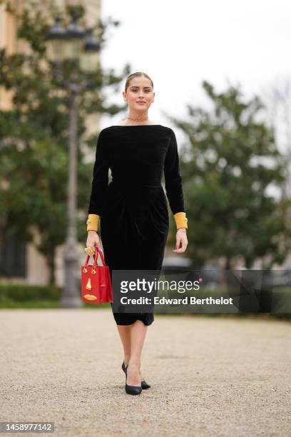 Valentina Ferragni wears a gold large pendant chain back necklace, a black velvet with gold sleeves long midi dress, a gold oversized ring, a red...