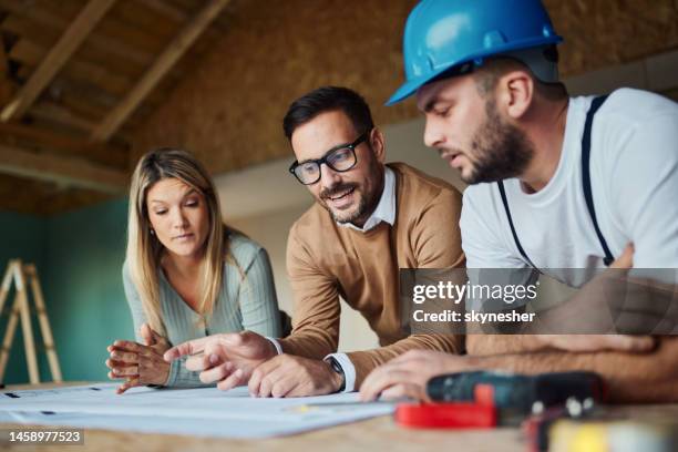 young couple analyzing blueprints with their construction worker/ - building contractor stockfoto's en -beelden