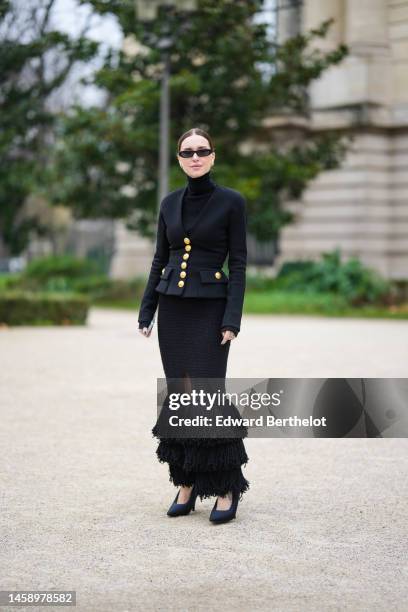 Pernille Teisbaek wears black sunglasses, silver and gold diamonds earrings, a black turtleneck pullover, a black with gold buttoned blazer jacket...