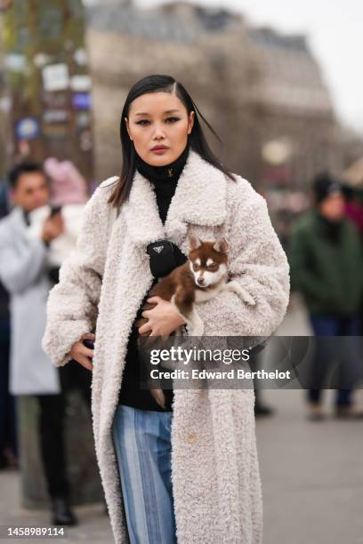 Guest wears a black turtleeck pullover, a white sheep fur long coat, blue striped print pattern faded denim large pants, a black crossbody bag from...