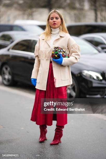 Guest wears gold earrings, a white wool turtleneck pullover, a beige fringed wool coat, a brown LV monogram print pattern in coated canvas with...