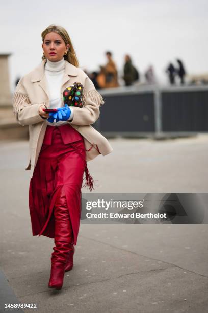 Guest wears gold earrings, a white wool turtleneck pullover, a beige fringed wool coat, a brown LV monogram print pattern in coated canvas with...