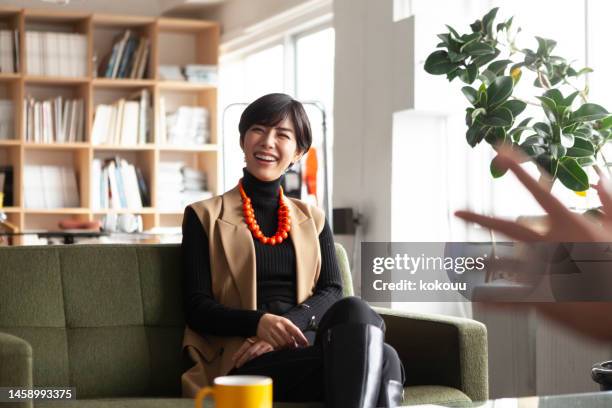 young businesswoman chatting with colleagues in a creative office. - 50 year old japanese woman stock pictures, royalty-free photos & images