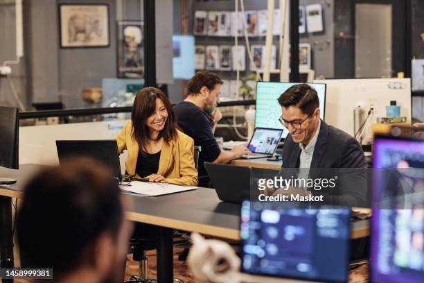 happy male and female business colleagues with laptop working at desk in office - economy business and finance imagens e fotografias de stock