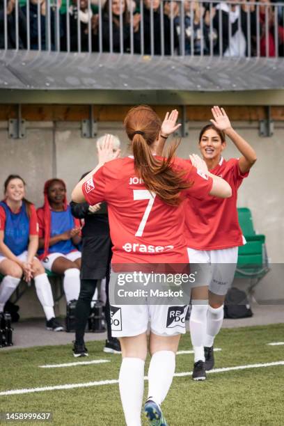 happy female soccer players giving high five while running towards each other in stadium - replaces stock-fotos und bilder