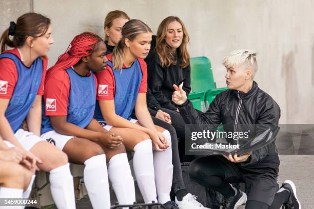 mature coach gesturing while talking to reserve female soccer players sitting together in dugout - reserve athlete - fotografias e filmes do acervo