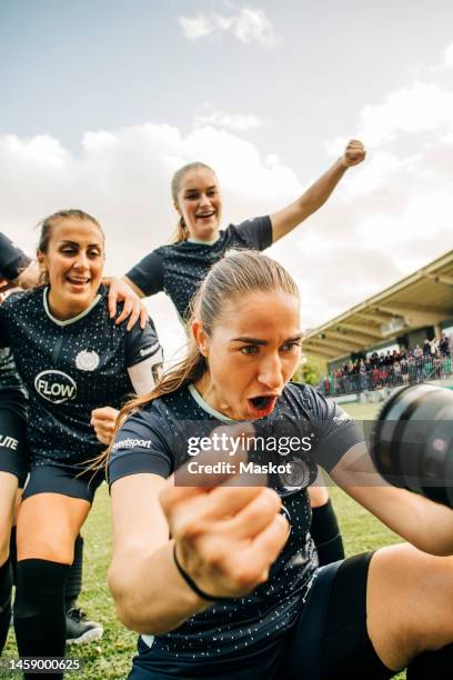 cheerful female players celebrating goal while looking at camera during match in soccer stadium - soccer championship stock pictures, royalty-free photos & images