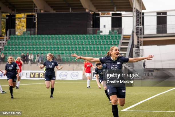 female soccer player running with arms outstretched after scoring goal in stadium - soccer competition stock pictures, royalty-free photos & images