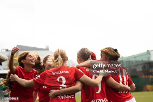 excited female soccer players huddling and celebrating win together in stadium - fútbol femenino fotografías e imágenes de stock