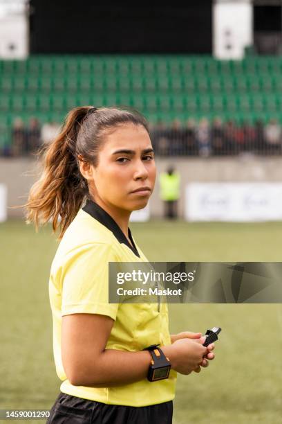 side view of young female referee holding whistle while standing in soccer stadium - árbitro imagens e fotografias de stock
