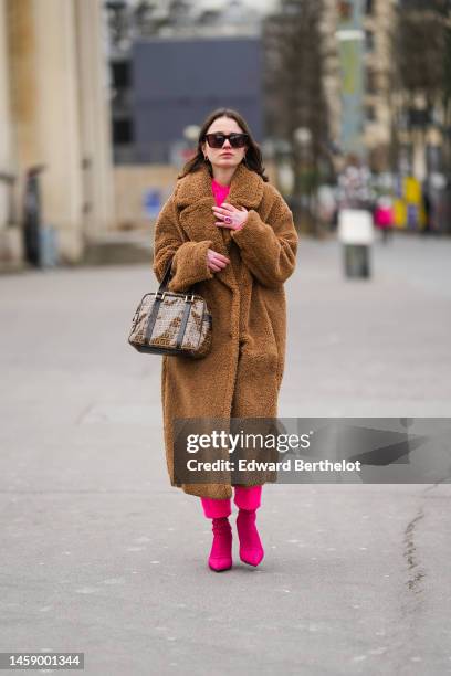 Guest wears black sunglasses, a neon pink pullover, matching neon pink suit pants, a brown sheep fur long oversized coat, a brown shiny leather FF...