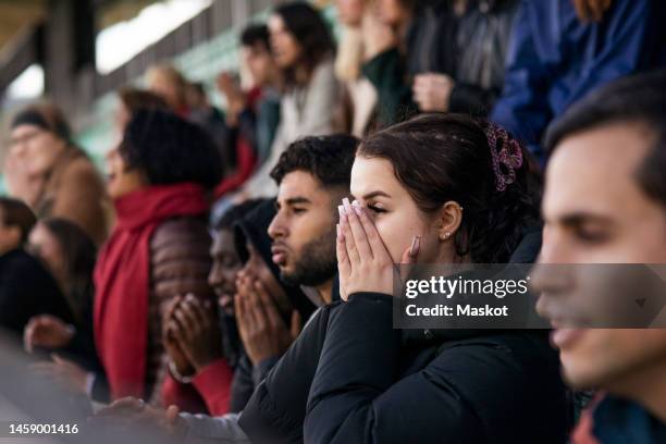 woman in audience covering mouth with hands while watching match at soccer stadium - football crowd stock pictures, royalty-free photos & images