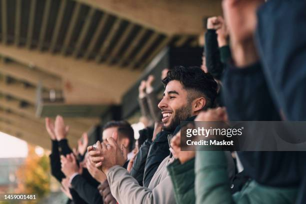 happy male fan in audience applauding while watching soccer match in stadium - hincha fotografías e imágenes de stock