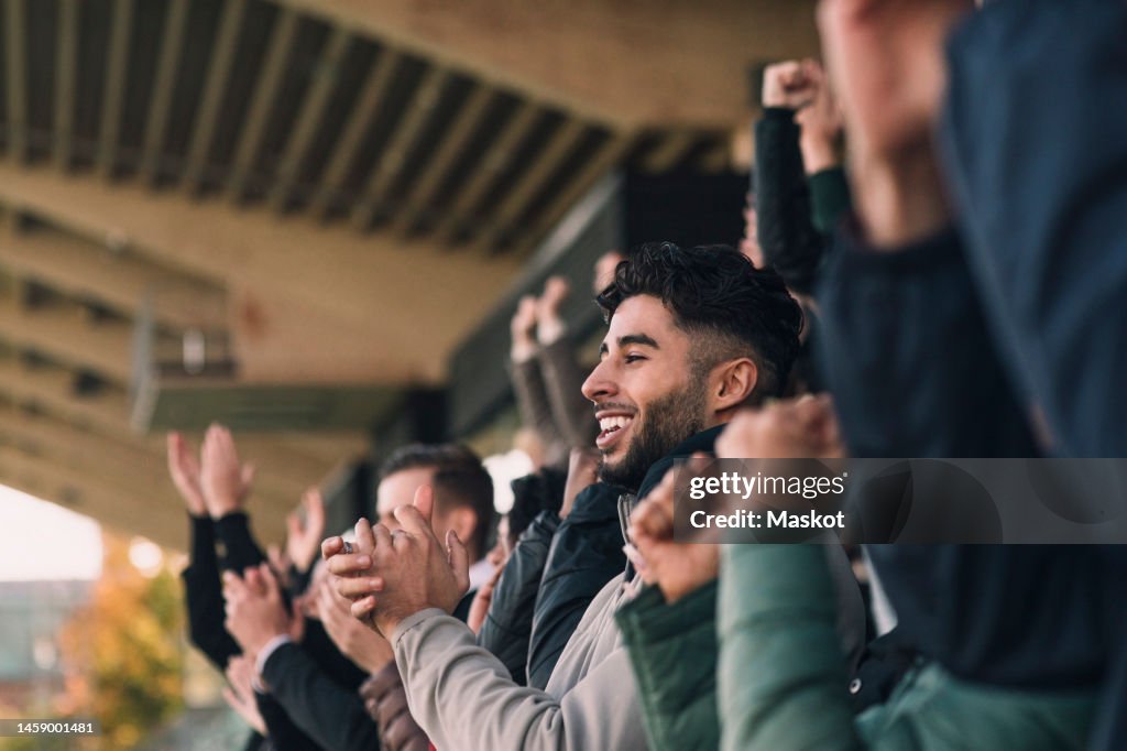Happy male fan in audience applauding while watching soccer match in stadium
