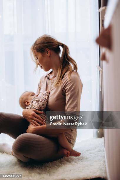 the young mother breastfeeding her baby girl at home - breastfeeding stock pictures, royalty-free photos & images
