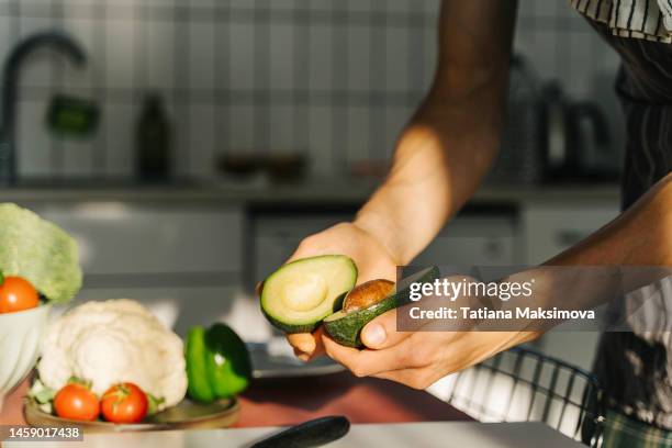 young man cooking guacamole in light kitchen at home. hands close-up. - avocado stock-fotos und bilder