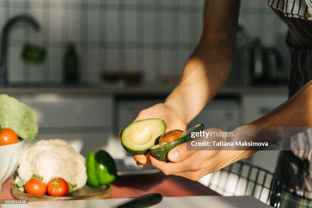 Young man cooking guacamole in light kitchen at home. Hands close-up.