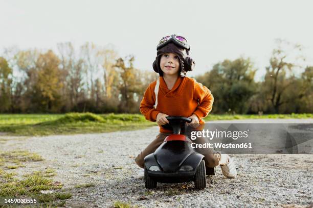 boy wearing flying goggles playing with bobby car - bobbycar stockfoto's en -beelden