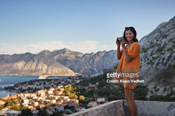 young woman with camera against mountains - town orange stock-fotos und bilder