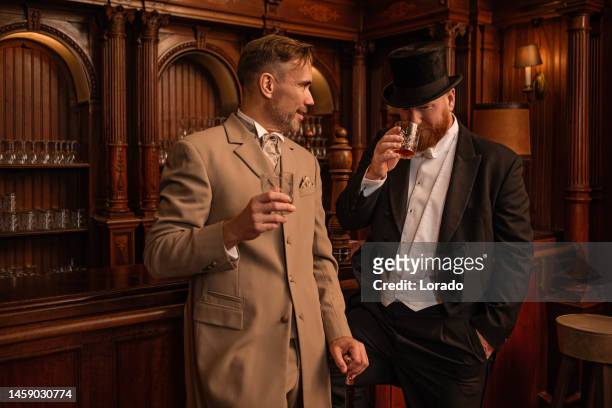 two handsome 1920s style gentlemen in a luxury brown bar - gentlemens club stock pictures, royalty-free photos & images