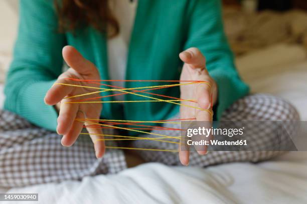 hands of woman playing cats cradle game at home - mani fili foto e immagini stock