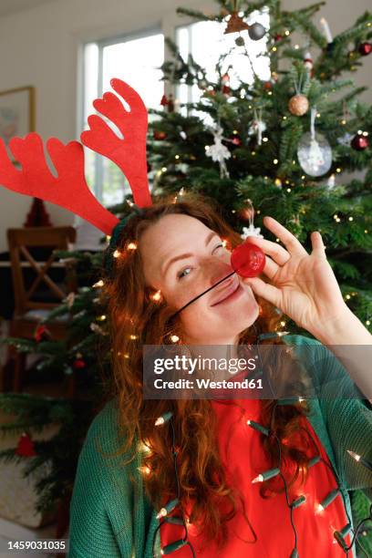smiling woman wearing clowns nose with christmas lights at home - antler stock pictures, royalty-free photos & images