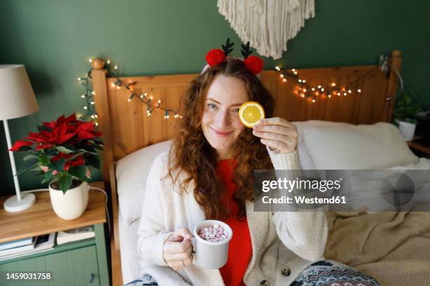 smiling woman holding cup of hot chocolate with marshmallows sitting on bed at home - hot arabic women 個照片及圖片檔