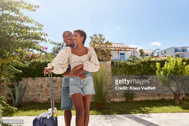 man embracing girlfriend in back yard on sunny day - suitcase couple stock-fotos und bilder