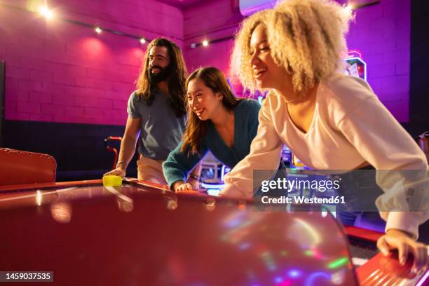 happy friends having fun playing air hockey at amusement arcade - hockey arcade game stock pictures, royalty-free photos & images
