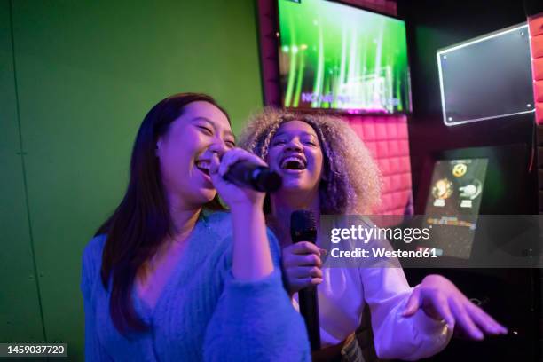 happy young friends singing karaoke in microphone at amusement arcade - karaoke stock pictures, royalty-free photos & images