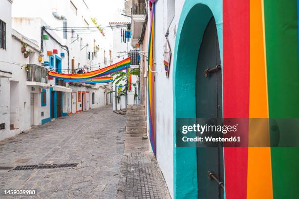 spain, balearic islands, ibiza, rainbow flags hanging over town alley - ibiza town stock pictures, royalty-free photos & images