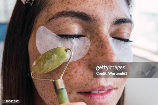 woman with freckle face massaging using jade stone roller - lichaamsverzorging stockfoto's en -beelden