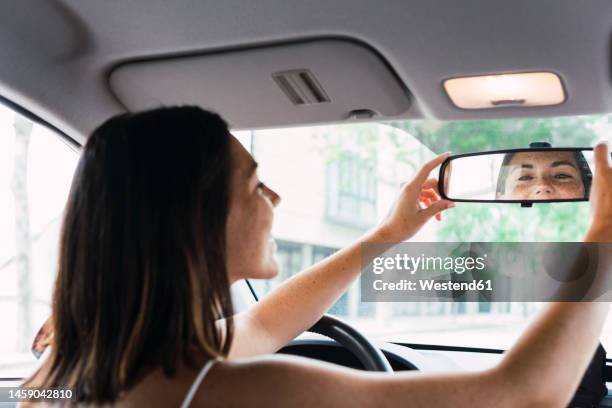 young woman adjusting rear view mirror in car - vehicle mirror stock pictures, royalty-free photos & images