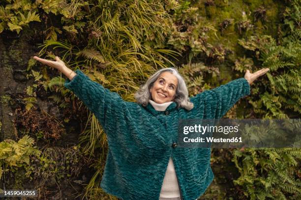 carefree senior woman with arms outstretched standing in front of plants - westend 61 fotografías e imágenes de stock