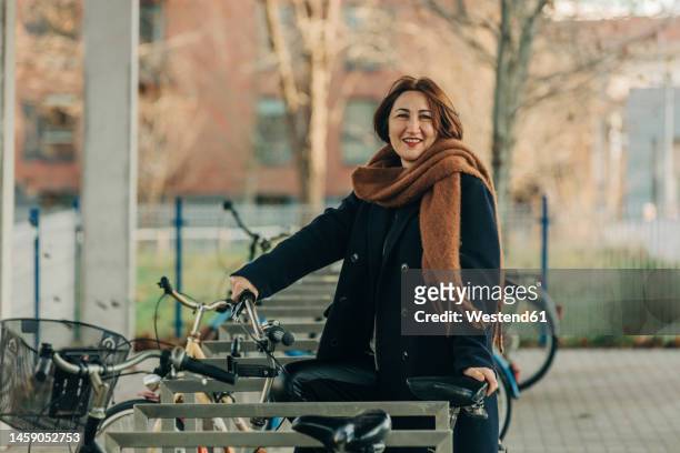 smiling mature woman with bicycle at parking station - mature woman winter stockfoto's en -beelden